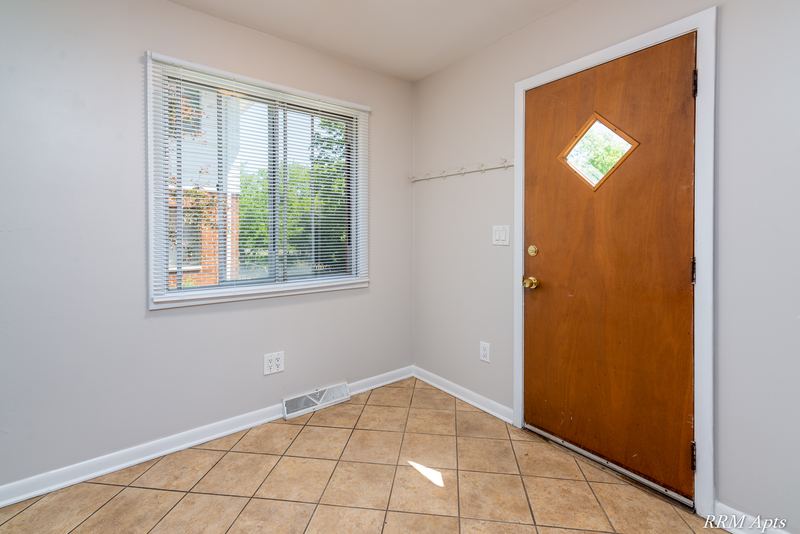 Dining area with beige tile floor, window and wood entry door with diamond window, Westerfield Place apartment 147B