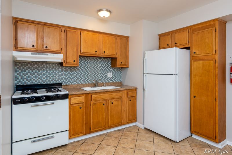 Kitchen with oak cabinets, white gas stove, white refrigerator and blue tile backsplash, Westerfield Place apartment 147B