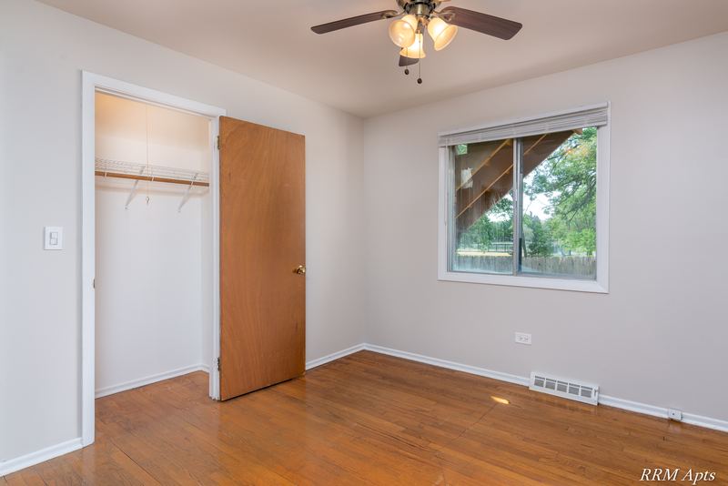 Bedroom with wood floor, ceiling fan, open closet with shelf and window facing trees, Westerfield Place apartment 147B