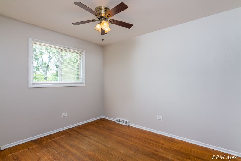 Bedroom with wood floor, ceiling fan, single window facing trees and baseboard radiator, Westerfield Place apartment 147B