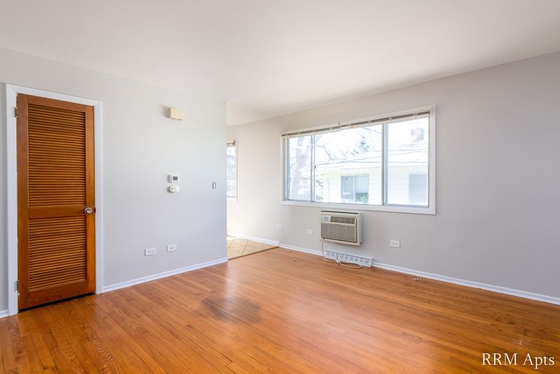 Living room with wood floor, wood entry door, window and a wall air conditioner, Westerfield Place apartment 149-C