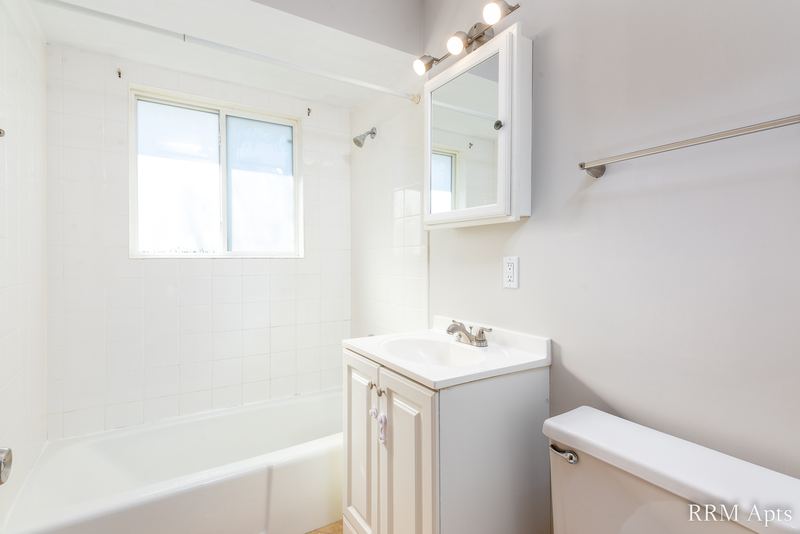Bathroom with white tub and tile surround, window, white vanity and mirrored cabinet, Westerfield Place apartment 149-C